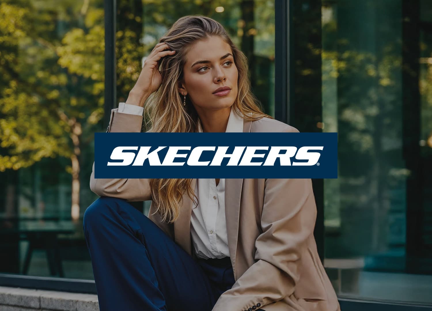 Frau mit langen, welligen Haaren in einem beigen Blazer und einer weißen Bluse, die im Freien sitzt, die Hand im Haar, den Blick zur Seite gerichtet, mit einem Glasgebäude im Hintergrund. Das Logo der Marke SKECHERS ist im Vordergrund.