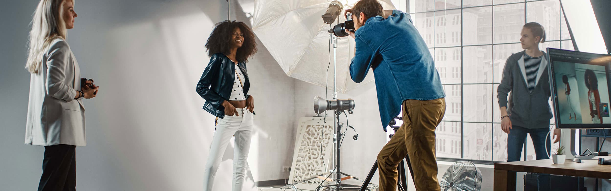 Ein Fotograf fotografiert ein posierendes Model in einem Studio mit Beleuchtungsausrüstung, während zwei Assistenten das Shooting beobachten.